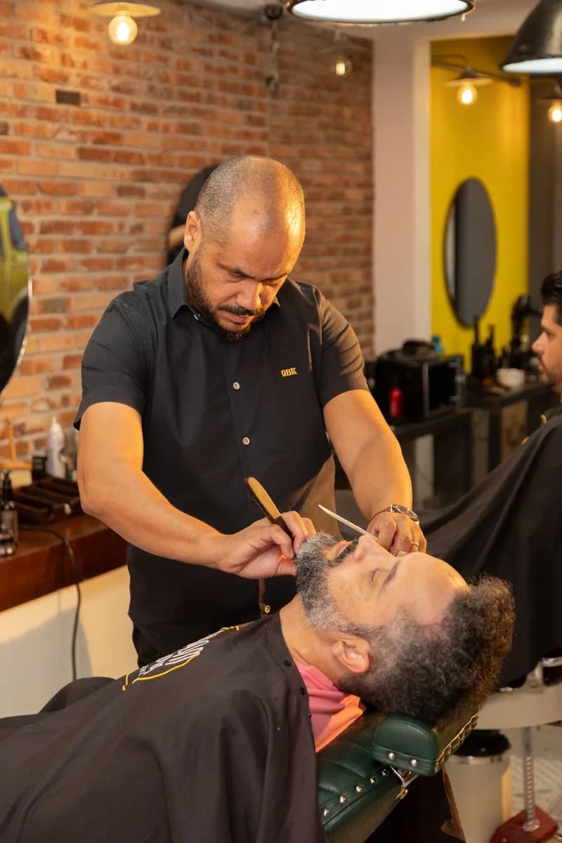 Barbeiro fazendo a barba de um cliente na O Bom Kbelo